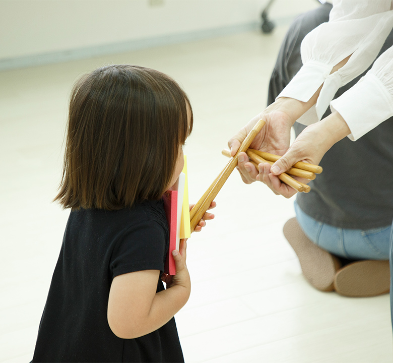 小さな楽器を先生と一緒に手に取るお子さま